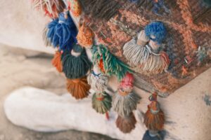 Vibrant and textured close-up of a camel saddle blanket with colorful tassels, exuding warmth and cultural richness.